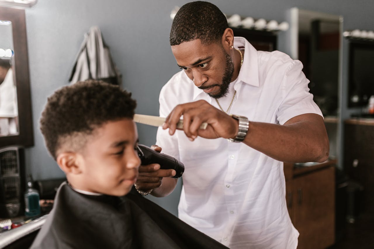 Barber in a white shirt carefully trimming a boys hair at a salon.